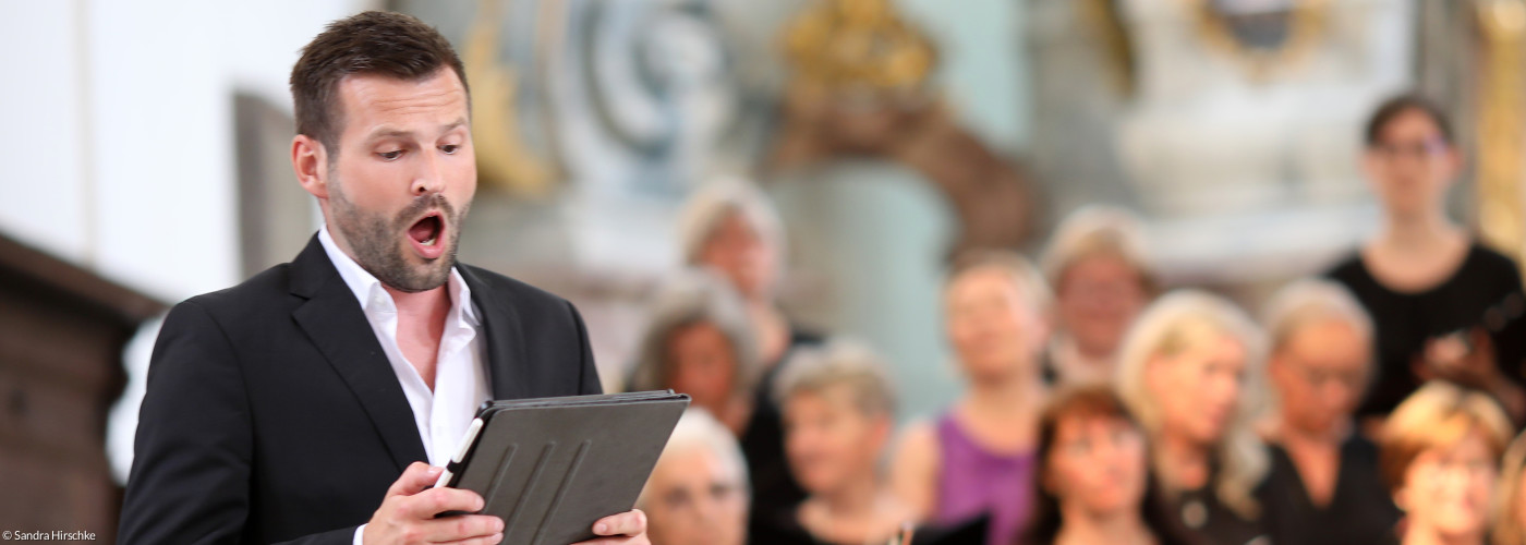 Ein Sänger steht singend vor einem Orchester